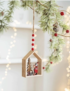 Hanging wooden house ornament with XMAS text, Santa Claus, and tree on pine branch