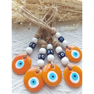 Detail of five orange evil eye charms with twine ropes on a white lace and hay background