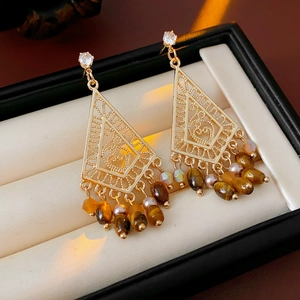 Detailed shot of golden geometric tassel earrings with zircon and tiger eye stones