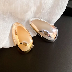 Macro shot of minimalist gold and silver oval brooches with high-polish mirror finish