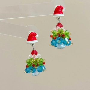 Close-up of handmade beaded Christmas tree earrings with red bows and colorful crystals