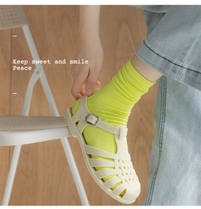 Detailed view of cream woven Roman sandals paired with vibrant neon green ribbed socks
