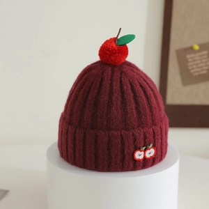 Detail of burgundy ribbed knit hat featuring cute apple pom-pom and embroidery