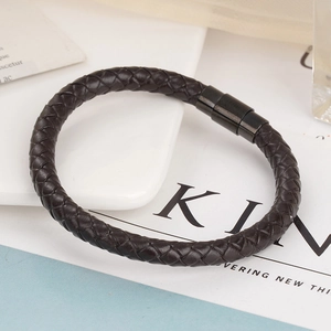 Close-up of a dark brown braided leather bracelet with black magnetic metal clasp on desk