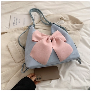 Detail of light blue handbag featuring a large pink velvet bow and metal chain strap