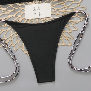 Detail view of black bikini bottoms with leopard print side ties on a decorative mat