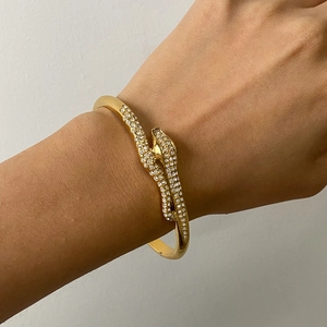 Detailed view of gold snake-shaped bangle with sparkling white crystals on model wrist