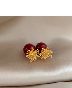 Macro shot of gold starburst earrings with red pearls on champagne silk fabric