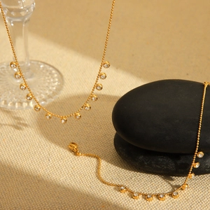 Detail of gold bead chain necklaces with clear zircon charms on textured fabric