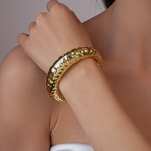 Detail of a gold hammered metal bracelet featuring unique irregular textures on model wrist
