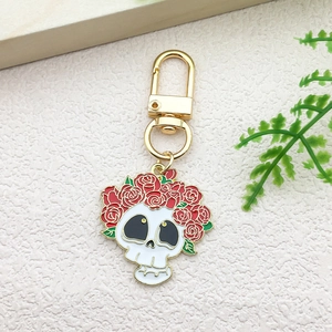 Detail of metal skull keychain decorated with red roses and green leaves on gold clasp