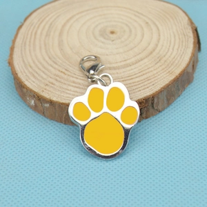 Detail view of a yellow paw print charm with metal lobster clasp on a wooden base