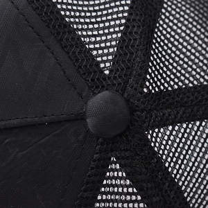Detailed close-up of the black trucker hat featuring mesh fabric and top button stitch detail