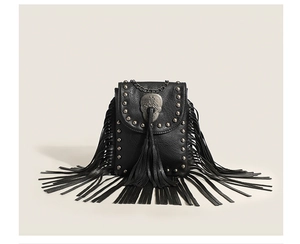 Detail of punk style crossbody bag featuring silver skull, studs and long black fringe