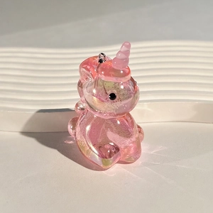 Iridescent pink acrylic unicorn keychain with bubbles and a metallic ring on a wave stand