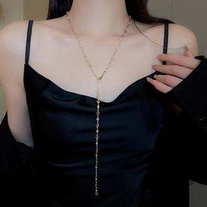 Detail view of a long gold Y-shaped tassel necklace with heart charms on a model