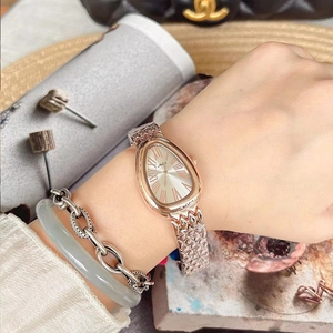 Close-up of a rose gold snake-head watch with a textured metal bracelet on a wrist