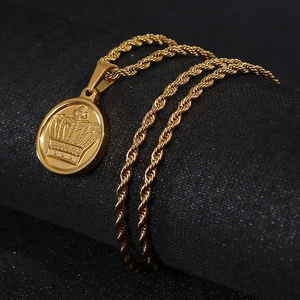 Detail view of a gold-plated crown pendant and twisted rope chain against a black background