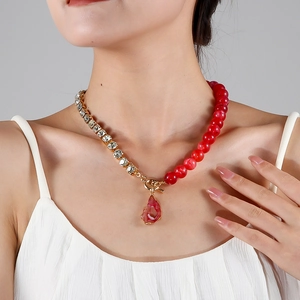 Nahaufnahme einer asymmetrischen Halskette mit Goldkette, Strass und rotem Steinanhänger