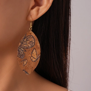 Detail of leaf-shaped cork earrings with black butterfly patterns and gold fish hooks