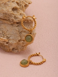 Detail of twisted gold hoop earrings with green natural agate stones on a textured rock