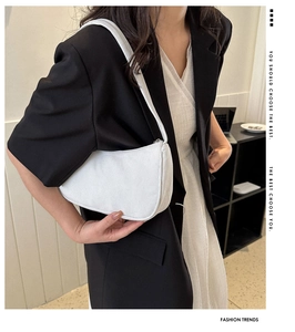 White corduroy baguette bag worn over the shoulder in a minimalist urban setting