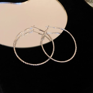 Detailed close-up of silver geometric hoop earrings with textured metallic finish