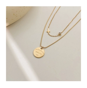 Detail of double-layer gold necklace featuring a cross and engraved round pendant