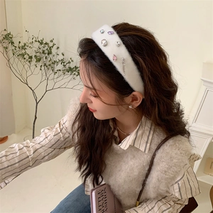 Detail of white plush headband with rhinestones worn by a model in a warm indoor setting