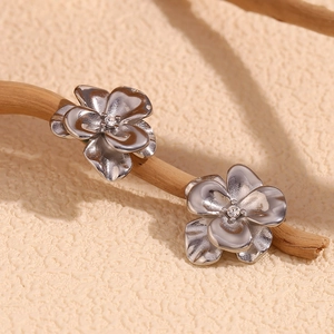 Macro shot of silver flower earrings with center crystal on a wooden branch