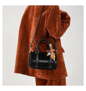 Side view of black Boston bag with decorative printed scarf handle on rust red jacket