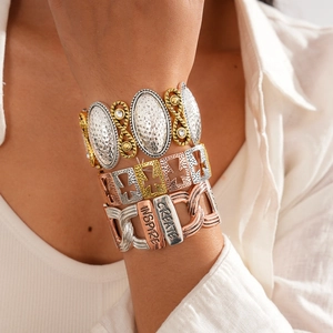 Close-up of bohemian stacked metal bangles with cross cutout and engraved inspire text