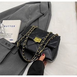 Close-up of black quilted small square bag with gold chain strap and turn-lock closure