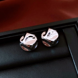 Close-up of silver-toned crumpled geometric stud earrings on a black leather tray
