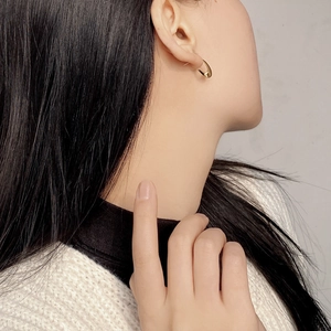 Close-up of minimalist gold U-shaped oval stud earring worn by a model in soft light