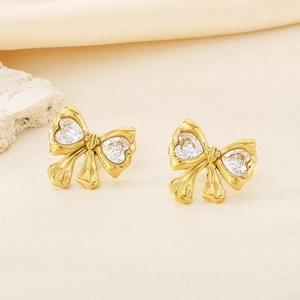 Detail of 18K gold bow stud earrings with heart-shaped sparkling crystals on stone base