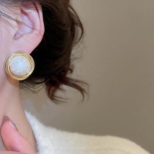 Close-up of gold-plated wrinkled geometric pearl stud earrings on a female model