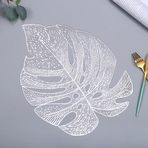 Detail of silver monstera leaf placemat with intricate hollowed veins on grey surface