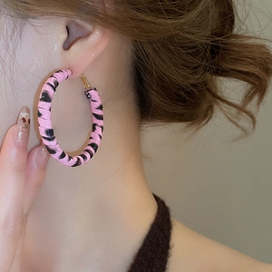 Gros plan de grandes boucles d'oreilles dorées avec motif zébré rose portées par mannequin