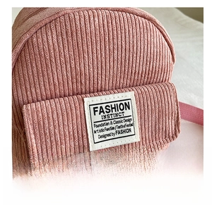 Close-up of pink corduroy fabric texture and minimalist white brand label on small backpack