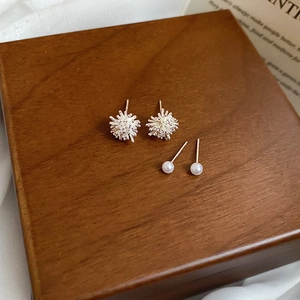 Detailed view of silver firework studs and white pearl earrings on a wooden box