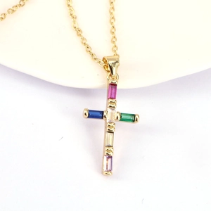 Gold cross necklace with colorful baguette-cut zircons on a white minimalist display