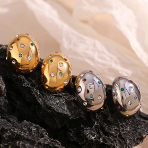 Macro detail of oval gold and silver earrings with colorful rhinestones on black stone