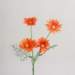Macro detail of orange artificial daisy flower with textured petals and green fern foliage
