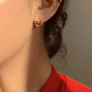 Gros plan d'une boucle d'oreille en forme de cœur doré porté sur une oreille féminine