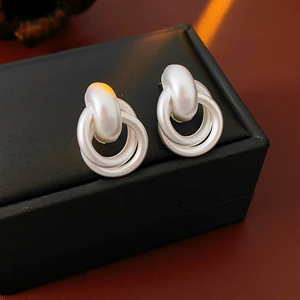 Detail of matte silver interlocking double loop earrings with center bead on a black box