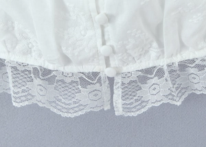 Détail de broderie florale, ourlet en dentelle et boutons recouverts sur haut en coton blanc