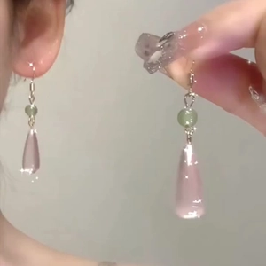 Close-up of pink resin teardrop earrings with green beads worn on ear for detail