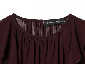 Détail du col à volants et étiquette de marque sur ce haut pour femme rouge foncé