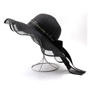 Détail d'un chapeau de paille à larges bords ondulés avec rubans en mousseline noire